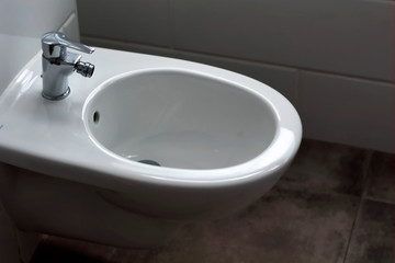white hanging bidet seat in the hotel home bathroom with white tiles and toilet paper on the wall. Bathroom luxury interior soft selective focus blurred