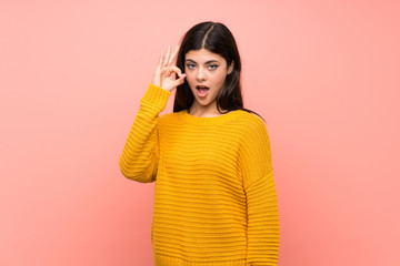 Teenager girl  over isolated pink wall surprised and showing ok sign