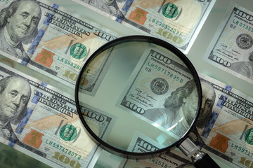 American money hundred dollar bills and magnifier on a glass background