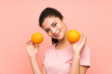 Fototapeta na wymiar Happy Teenager girl over isolated pink wall holding oranges