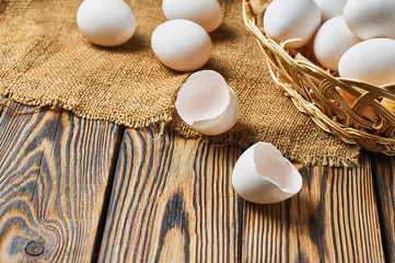 Basket with sawdust full of chicken eggs near shells lies on rustic wooden table. Space for text