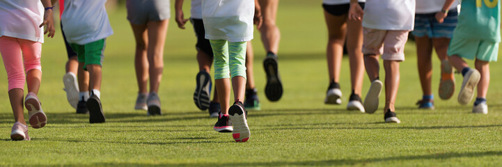 Fototapeta premium Running children, young athletes run in a kids run race, running on grass detail on legs, running in the light of morning