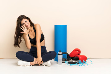 Teenager sport girl sitting on the floor counting five with fingers