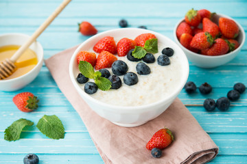 Healthy Breakfast of oatmeal with fresh strawberries, blueberries and honey on a blue background.