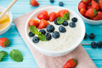 Healthy Breakfast of oatmeal with fresh strawberries, blueberries and honey on a blue background.