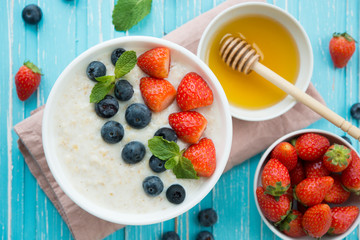 Healthy Breakfast of oatmeal with fresh strawberries, blueberries and honey on a blue background. Top view
