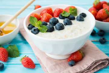 Healthy Breakfast of oatmeal with fresh strawberries, blueberries and honey on a blue background.