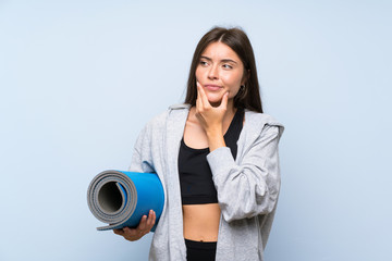 Fototapeta premium Young sport girl with mat over isolated blue background thinking an idea