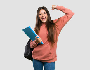 Young student woman holding notebooks celebrating a victory over isolated grey background