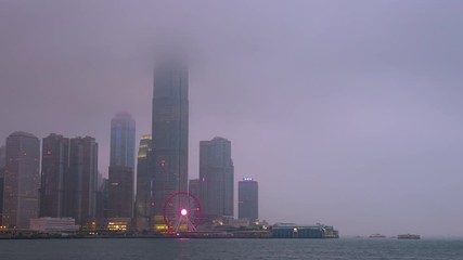 Time lapse day to night of Hong Kong cityscape with hard mist at the harbor in the raining day