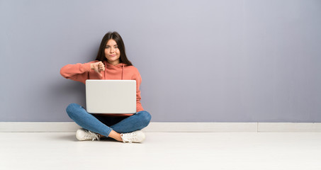 Young student girl with a laptop on the floor showing thumb down sign