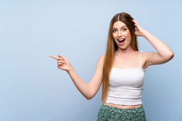 Young woman over isolated blue background surprised and pointing finger to the side