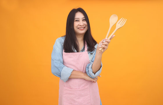 Happy Asian woman is cooking with apron for cooking advertise theme on on yellow background.