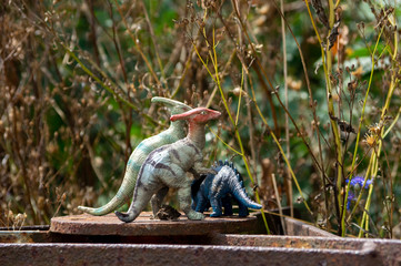 group of small toy parasaurolophus dinosaurs standing in a garden in front of high grass