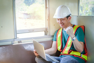 The young engineer holds a notebook computer sitting on a moving train. Raise arms to be happy with the work that is accomplished.
