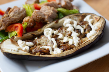 Cooked, baked eggplant stuffed with cheese, nuts, and yogurt dressing with fresh salad, in white plate. Healthy food.