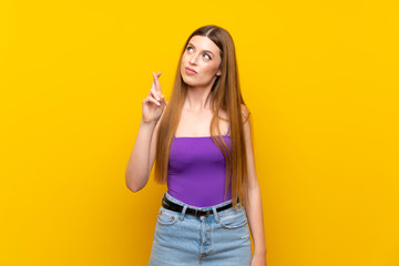 Young woman over isolated yellow background with fingers crossing and wishing the best
