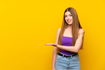 Young woman over isolated yellow background presenting an idea while looking smiling towards
