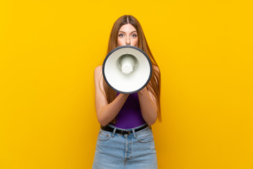 Young woman over isolated yellow background shouting through a megaphone