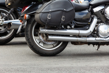 rear part of a motorcycle: wheel, exhaust pipe and black leather wardrobe trunk (luggage bag) close-up, side view