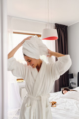 Young pretty smiling woman in white bathrobe and towel on head happily looking down while girl...