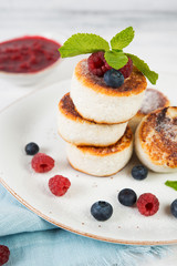 Fried curd cheesecakes decorated with fresh berries and mint. Vertical orientation.