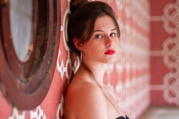 Portrait of young pretty woman leaning on pink designed wall with white ornament and looking at camera