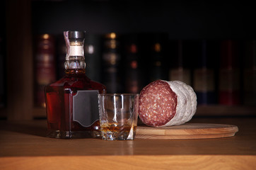 bottle of whiskey with glass of salami on oak table