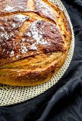 A loaf of sourdough bread freshly baked and standing on a mat ready to be sliced and eaten.