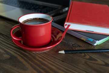 Red cup of fresh aroma morning coffee, laptop and book on wooden table