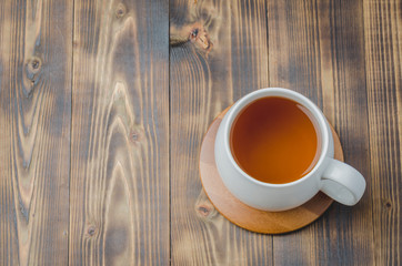 white cup with tea on a bamboo support on a wooden table, top view, copyspace