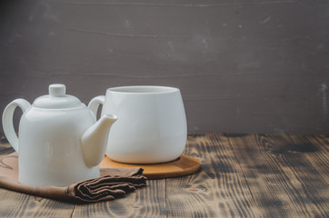 white cup of tea and teapot on a black wooden background, selective focus and copyspace