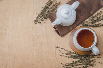 Thyme herbal tea in a white cup and teapot on a wooden table. Copyspace and top view