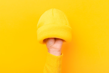 Hand with knitted wool hat, head accessory clothing over yellow trendy background