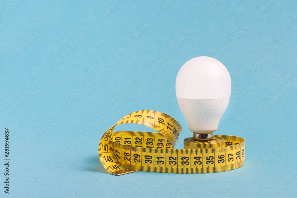 Wall mural Measuring tape wrapped around a light bulb on a blue background. Minimum creative concept, the concept of the idea of excess weight and a healthy lifestyle.