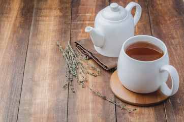 Thyme herbal tea in a white cup and teapot on a wooden table. Copyspace