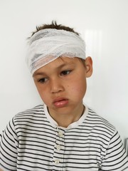 Sad young boy with bandage on his head. gray background