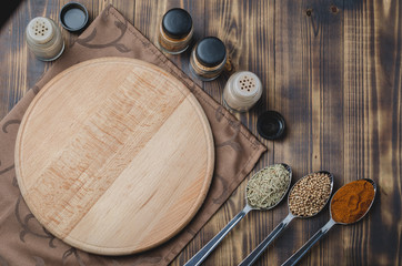 Various spices in spoons, cutting board and cooking utensils on wooden background. Top view