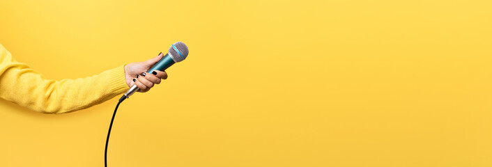 hand holding microphone over yellow background, panoramic mock up image - obrazy, fototapety, plakaty