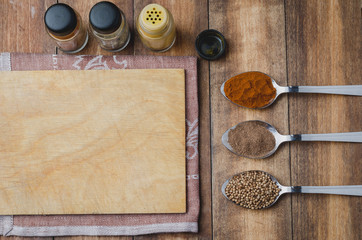 Various spices in spoons, cutting board and cooking utensils on wooden background. Top view