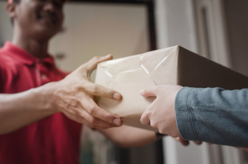 young delivery service man in red uniform smiling with woman customer receiving parcel post box from courier at home, cargo shipping, express delivery service, online shopping and logistics concept