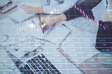 A woman hands writing information about stock market in notepad. Forex chart holograms in front. Concept of research. Double exposure