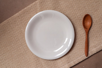 White plate and wooden spoon on cream tablecloth ready to eat