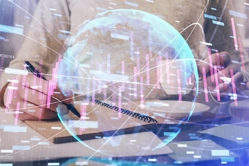 Forex chart hologram on hand taking notes background. Concept of analysis. Double exposure