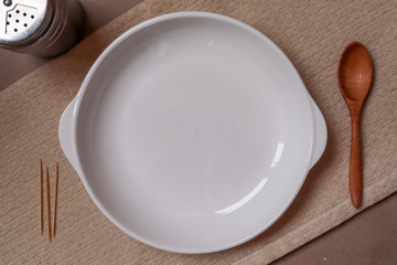 White plate and wooden spoon and spice jar on cream tablecloth ready to eat