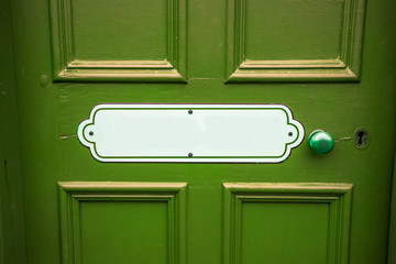 Old blank oval vintage metal painted sign with copy space on a painted green wooden background with matching door handle