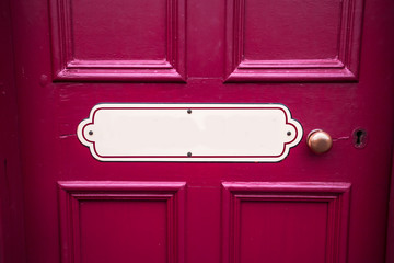 Old blank oval vintage metal painted sign with copy space on a painted purple wooden background with brass door handle
