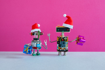 Small and big robots dressed as Santa Claus with bags of gifts wish a Merry Christmas and Happy New...