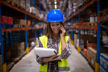 Portrait of beautiful female warehouse worker having conversation on cell phone in large storage...
