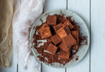 handmade souffle cubes covered with cocoa powder and pieces of chocolate lie on a plate on a light wooden table.
